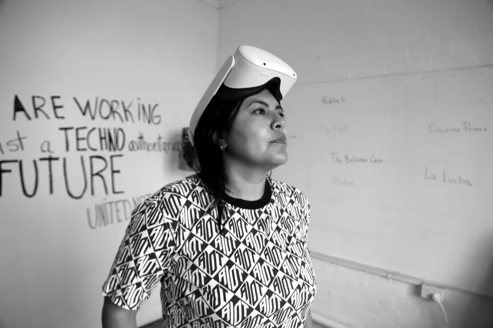A woman with a VR headset on her forehead, before a wall with the words: we are working against a techno authoritarian future.