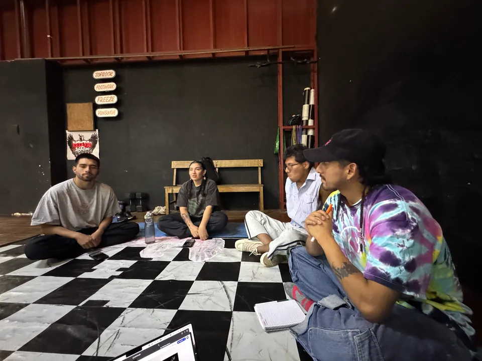 Four members of the team sit on the checkered floor of El Martadero, with notebooks, under a red roof.